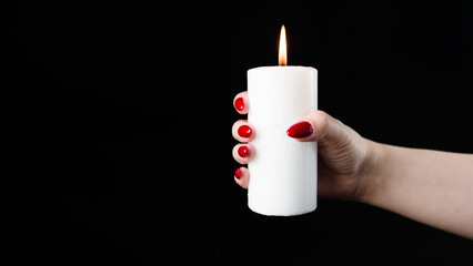 Crop woman with burning candle in studio. Crop female with red nails holding burning candle in hands against black background
