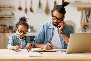 Young african american dad working remotely on laptop with child son at home - Powered by Adobe