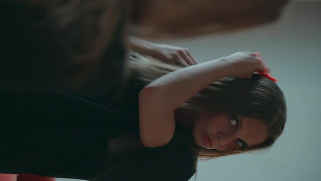 Caucasian girl in a black dress combs her hair. A European woman with blond hair stands in front of a mirror with a comb. The lady is going on a date.