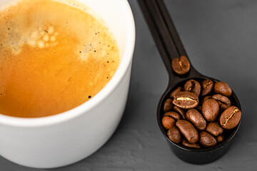 White cup of espresso coffee and coffee beans close-up. Coffee preparation.