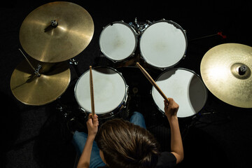 Top view of a boy learning to play the drums in the studio on a black background. A student of a...