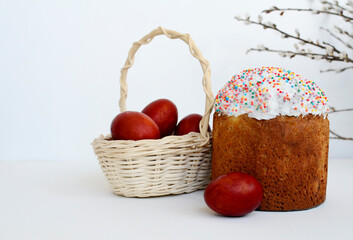 Easter cake, painted eggs in white basket, willow branches on white background with copy space.