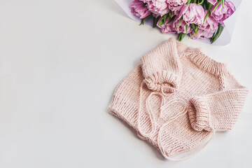 Knitted kids clothes and accessories for knitting. Needlework and knitting. Hobbies and creativity. Knit for children. Handmade. Pink sweater and tulips