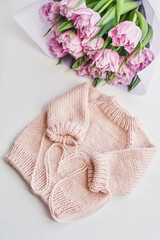 Knitted kids clothes and accessories for knitting. Needlework and knitting. Hobbies and creativity. Knit for children. Handmade. Pink sweater and tulips