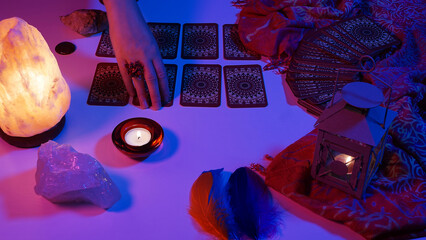 Woman turning over lined up tarot cards with her hand. Tarot card reading session. Cyberpunk blue pink neon light. Predicting the future, esoteric, mystic.