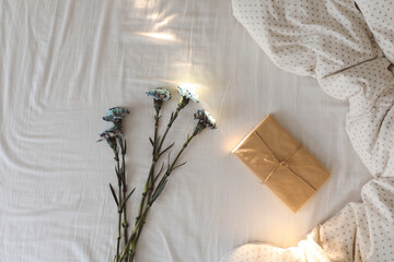 Bouquet of flowers and a gift covered in paper on crumpled white bed sheets