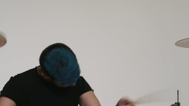 Caucasian guy with blue hair plays the drums. Yellow drum set. A drummer in black clothes plays on a white background. Close-up of a hi-hat.