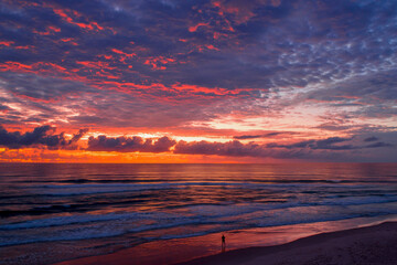 Fototapeta na wymiar Person standing on beach with a colorful sunrise sky