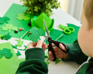 DIY St.Patricks Day decor. Happy boy make craft card of shiny green paper. Selective focus