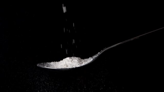 Flour falls in slow motion on a tablespoon isolated on black background