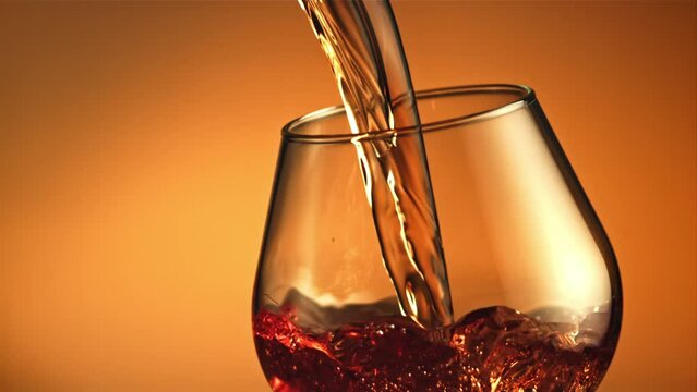 Cognac flows in a stream with air bubbles into the glass. On a brown background. Filmed is slow motion 1000 fps. High quality FullHD footage