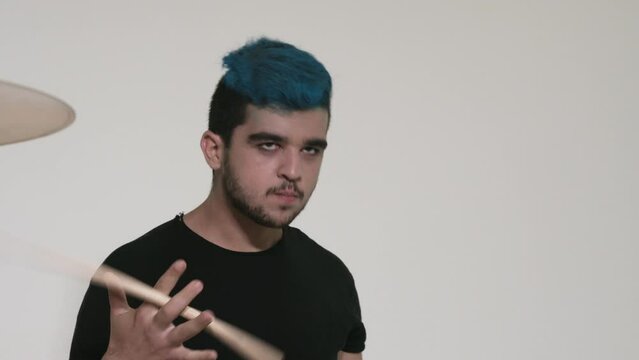 Caucasian guy with blue hair plays the drums. Yellow drum set. A drummer in black clothes plays on a white background. Close-up of a hi-hat.