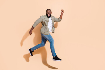 Fototapeta na wymiar Full body profile photo of hooray young brunet guy run yell wear shirt jeans shoes isolated on beige background