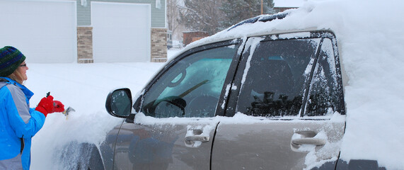 Female clearing winter snow off her car outside.
