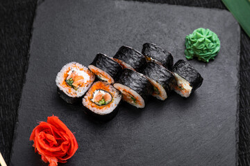 sushi rolls laid out on a dark background decorated with bamboo leaves and chopsticks