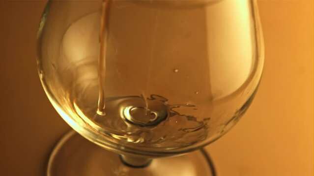 Cognac with splashes pours into the glass. On a brown background.Filmed is slow motion 1000 fps. High quality FullHD footage