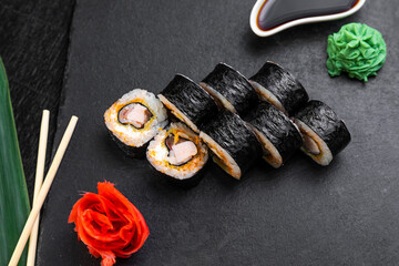 sushi rolls laid out on a dark background decorated with bamboo leaves and chopsticks