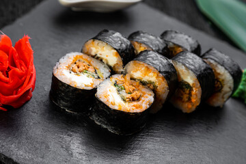 sushi rolls laid out on a dark background decorated with bamboo leaves and chopsticks