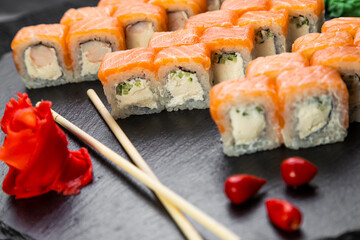 sushi rolls laid out on a dark background decorated with bamboo leaves and chopsticks