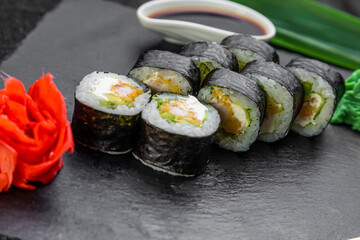sushi rolls laid out on a dark background decorated with bamboo leaves and chopsticks