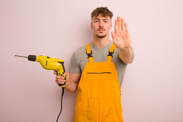 young cool man looking serious showing open palm making stop gesture. handyman and drill concept