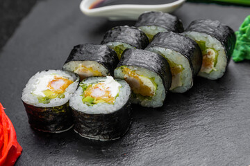 sushi rolls laid out on a dark background decorated with bamboo leaves and chopsticks