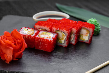 sushi rolls laid out on a dark background decorated with bamboo leaves and chopsticks