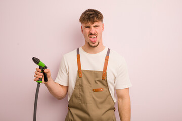 young cool man feeling disgusted and irritated and tongue out. gardener and hose concept