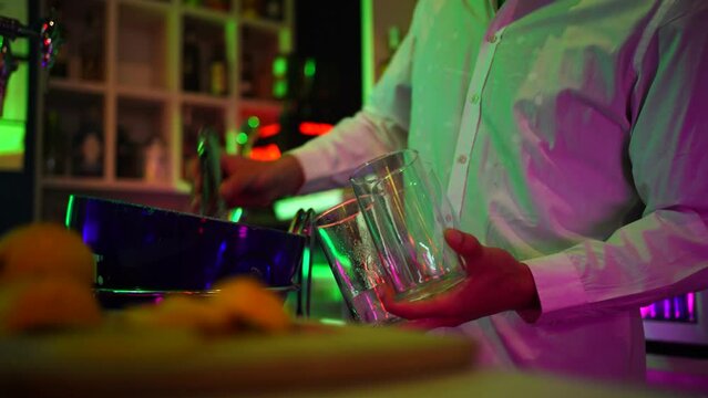 Manos de camarero sirviendo lim&oacute;n a tres copas en la barra de una discoteca con luces de ne&oacute;n. El fondo est&aacute; desenfocado.