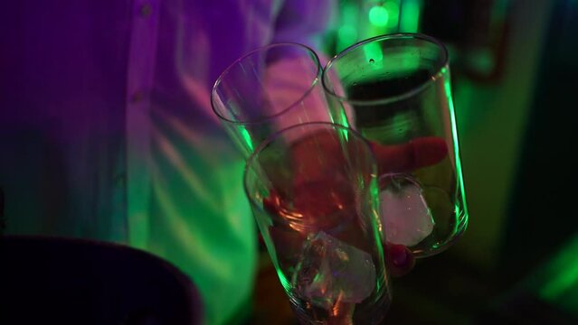 Manos de camarero sirviendo lim&oacute;n a tres copas en la barra de una discoteca con luces de ne&oacute;n. El fondo est&aacute; desenfocado.