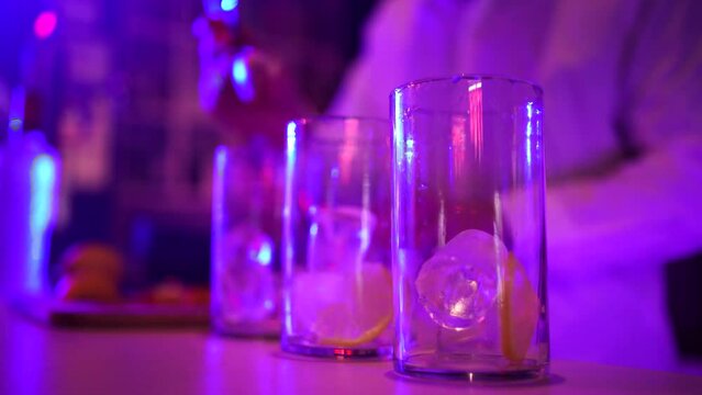 Manos de camarero sirviendo lim&oacute;n a tres copas en la barra de una discoteca con luces de ne&oacute;n. El fondo est&aacute; desenfocado.