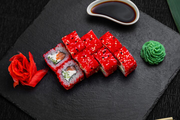 sushi rolls laid out on a dark background decorated with bamboo leaves and chopsticks