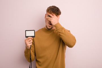 young cool man looking shocked, scared or terrified, covering face with hand. vip pass id concept