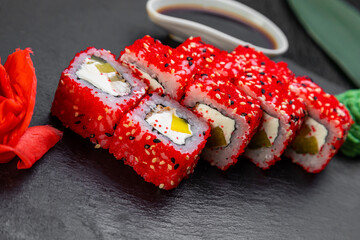 sushi rolls laid out on a dark background decorated with bamboo leaves and chopsticks