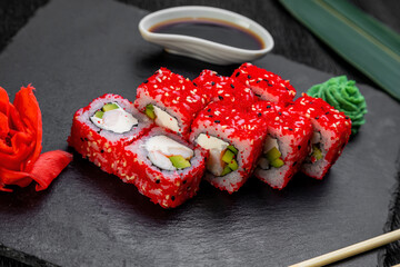 sushi rolls laid out on a dark background decorated with bamboo leaves and chopsticks