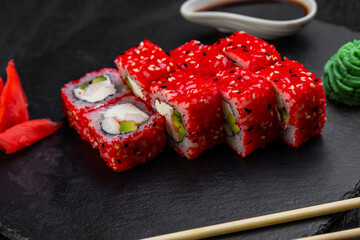 sushi rolls laid out on a dark background decorated with bamboo leaves and chopsticks