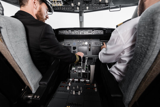 bearded pilot in cap using thrust lever near co-pilot in airplane simulator.