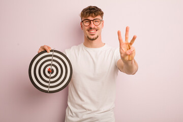 young cool man smiling and looking friendly, showing number three. dart target concept