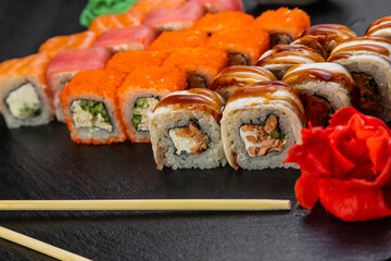 sushi rolls laid out on a dark background decorated with bamboo leaves and chopsticks