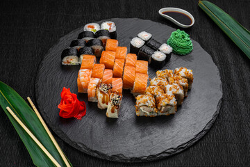 sushi rolls laid out on a dark background decorated with bamboo leaves and chopsticks