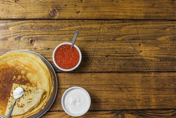 Pancakes with sour cream and caviar on a wooden background. Maslenitsa. Top view