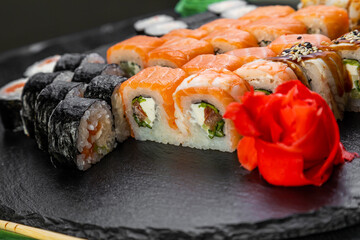 sushi rolls laid out on a dark background decorated with bamboo leaves and chopsticks