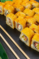 sushi rolls laid out on a dark background decorated with bamboo leaves and chopsticks