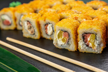 sushi rolls laid out on a dark background decorated with bamboo leaves and chopsticks