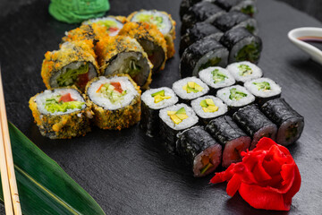 sushi rolls laid out on a dark background decorated with bamboo leaves and chopsticks