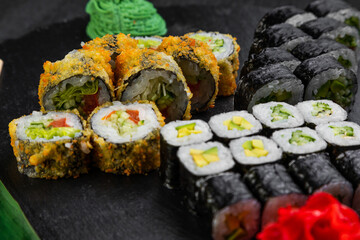 sushi rolls laid out on a dark background decorated with bamboo leaves and chopsticks