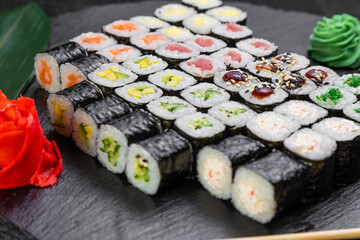 sushi rolls laid out on a dark background decorated with bamboo leaves and chopsticks