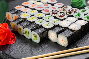 sushi rolls laid out on a dark background decorated with bamboo leaves and chopsticks