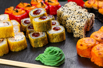 sushi rolls laid out on a dark background decorated with bamboo leaves and chopsticks