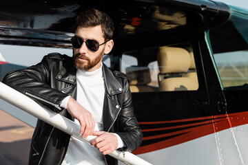 confident man in sunglasses and black leather jacket near helicopter.